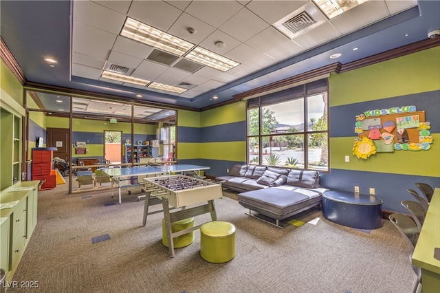 recreation room with a tray ceiling, carpet, visible vents, and crown molding