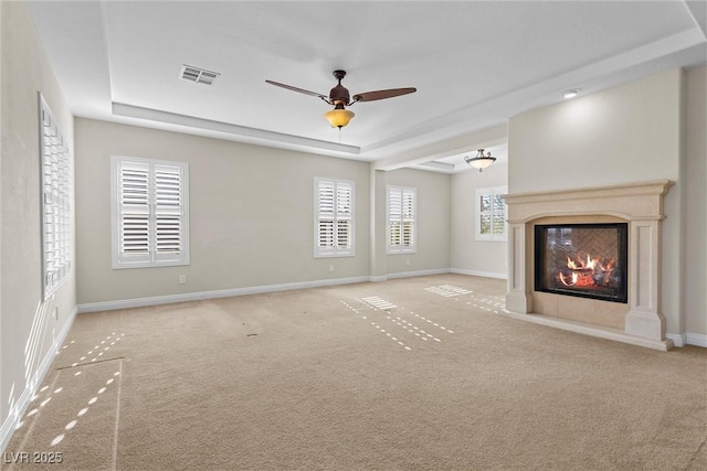 unfurnished living room with a tray ceiling, carpet flooring, visible vents, and baseboards