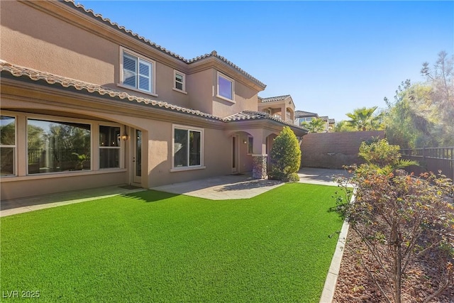 back of house featuring a tile roof, a patio, stucco siding, a lawn, and fence