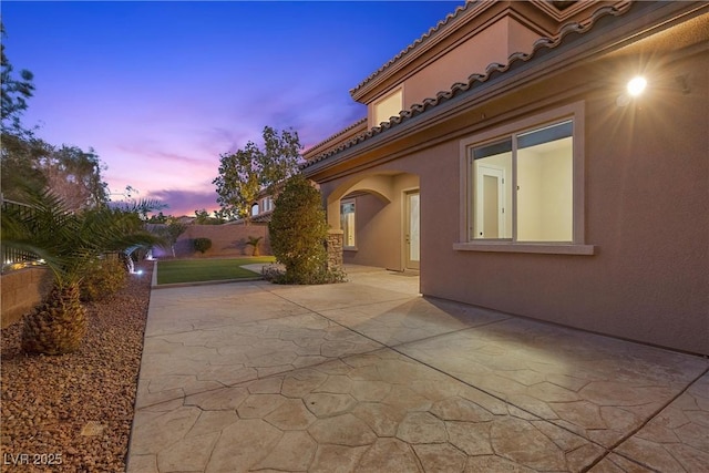 view of side of property with a patio area, a tiled roof, fence, and stucco siding