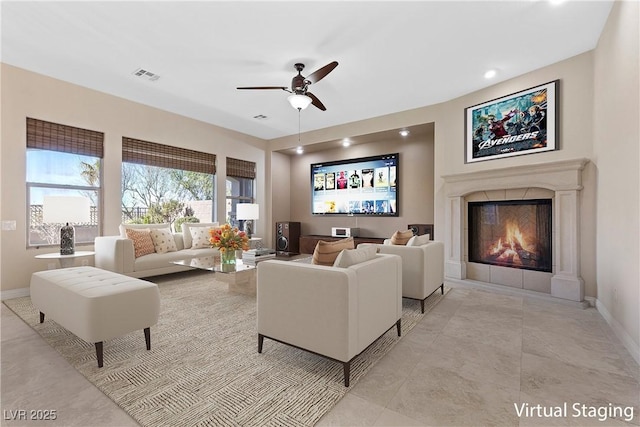 living area featuring baseboards, visible vents, ceiling fan, and a glass covered fireplace