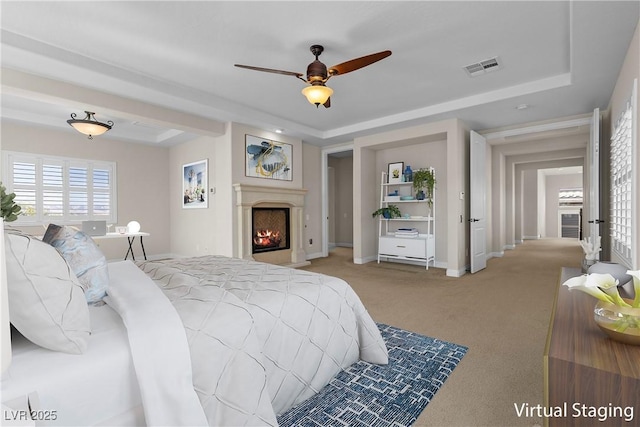 bedroom with a tray ceiling, visible vents, a lit fireplace, and carpet flooring