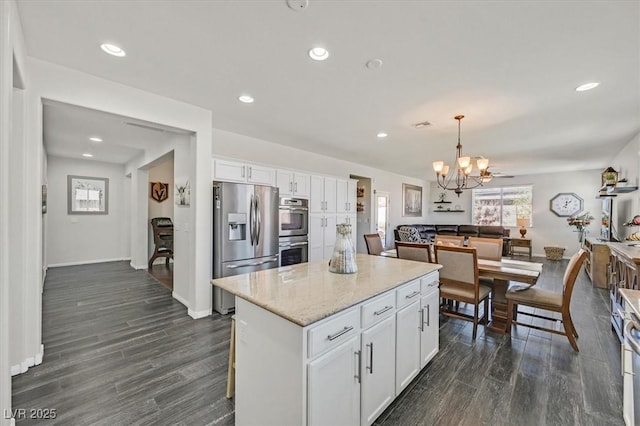 kitchen with appliances with stainless steel finishes, light stone countertops, white cabinets, a kitchen island, and decorative light fixtures