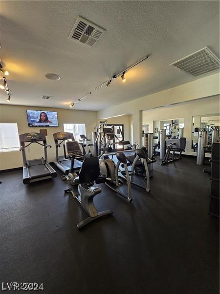 gym featuring a textured ceiling, track lighting, and a wealth of natural light