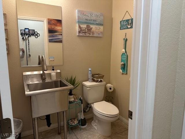 half bathroom with tile patterned flooring, toilet, baseboards, and a sink