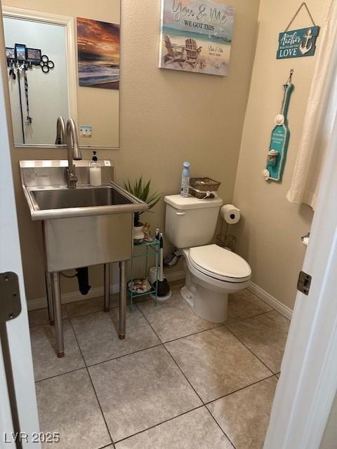 bathroom featuring tile patterned flooring, toilet, baseboards, and a sink