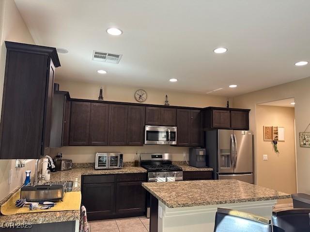 kitchen with dark brown cabinetry, sink, a center island, light tile patterned floors, and stainless steel appliances