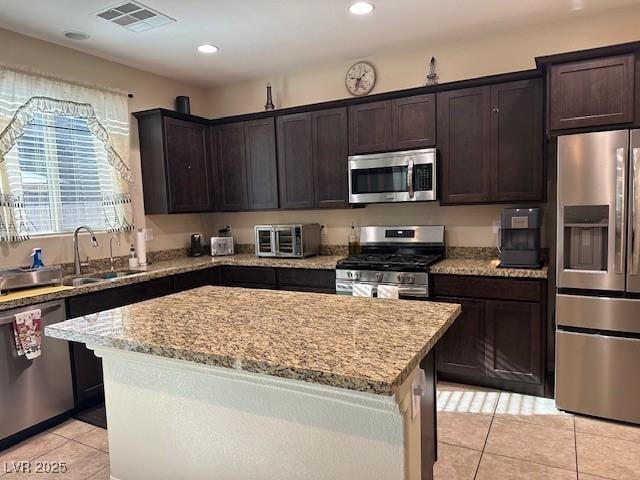 kitchen with light tile patterned floors, visible vents, dark brown cabinets, appliances with stainless steel finishes, and a center island