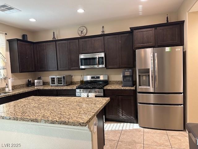 kitchen with dark brown cabinetry, appliances with stainless steel finishes, light stone countertops, and a kitchen island