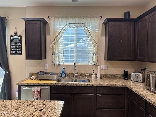 kitchen with light stone counters, dark brown cabinetry, dishwasher, and sink