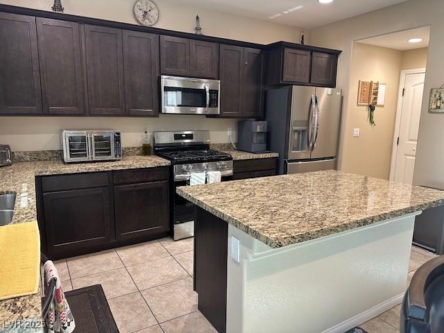 kitchen with appliances with stainless steel finishes, light stone countertops, dark brown cabinets, and light tile patterned floors