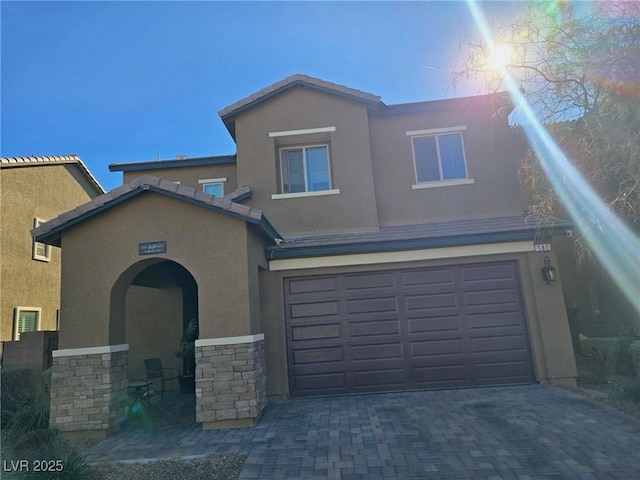 traditional-style home featuring a tiled roof, stucco siding, decorative driveway, stone siding, and an attached garage