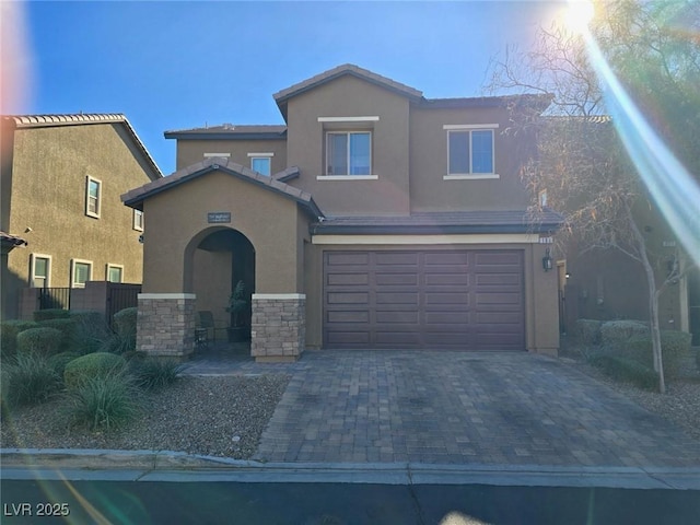 traditional-style home featuring stucco siding, decorative driveway, stone siding, fence, and a garage