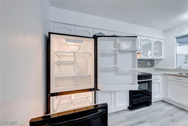 kitchen with white cabinets, black range, sink, and backsplash