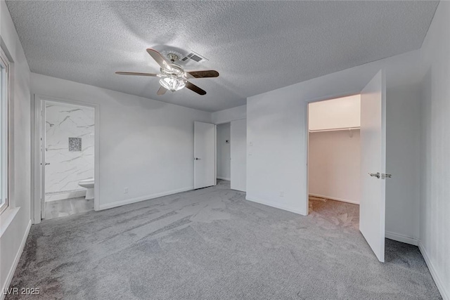 unfurnished bedroom with ceiling fan, ensuite bathroom, light colored carpet, a walk in closet, and a closet