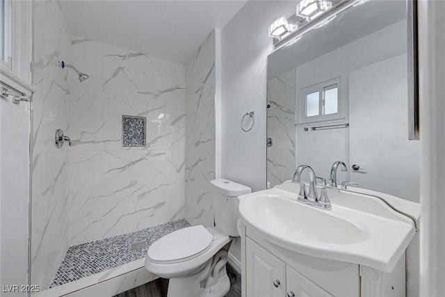 bathroom with a tile shower, vanity, and toilet