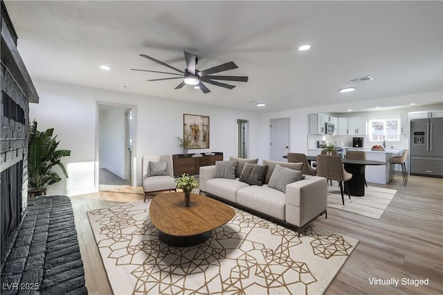 living room with a brick fireplace, ceiling fan, and light hardwood / wood-style floors