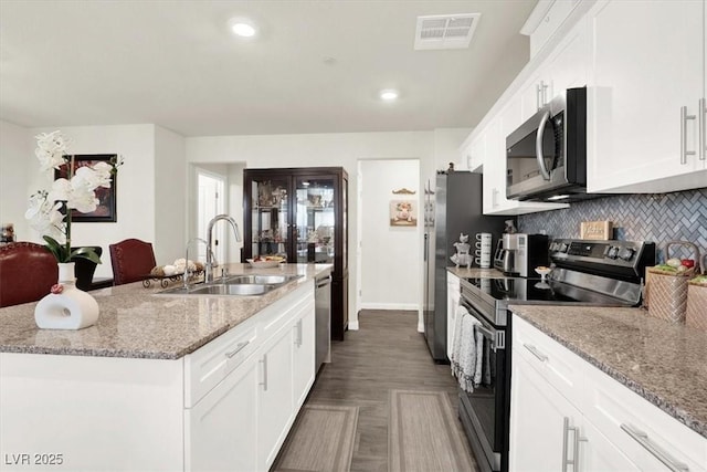 kitchen featuring a center island with sink, sink, white cabinetry, appliances with stainless steel finishes, and light stone counters