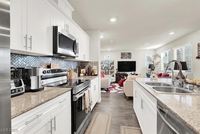 kitchen with white cabinets, stainless steel appliances, tasteful backsplash, sink, and light stone counters