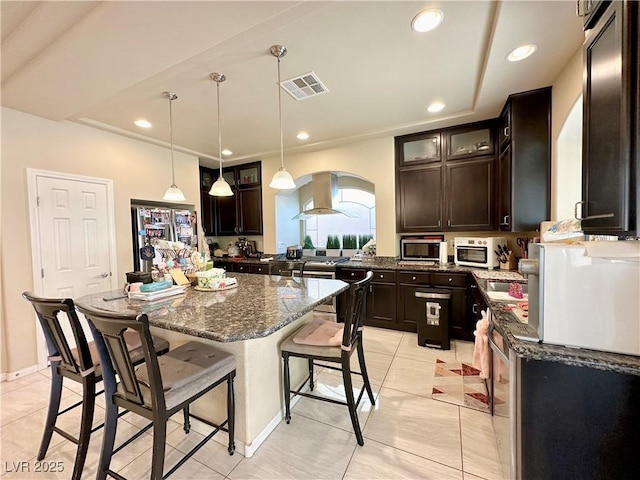 kitchen with a center island, hanging light fixtures, dark brown cabinets, light tile patterned flooring, and island exhaust hood