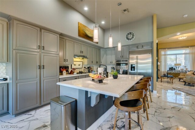 kitchen with backsplash, hanging light fixtures, a towering ceiling, appliances with stainless steel finishes, and a kitchen bar