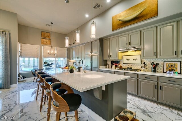 kitchen with an inviting chandelier, a towering ceiling, an island with sink, tasteful backsplash, and decorative light fixtures