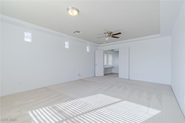 empty room featuring ceiling fan, a tray ceiling, and light carpet