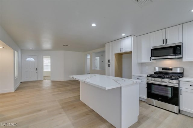 kitchen featuring a kitchen island, light stone countertops, appliances with stainless steel finishes, light hardwood / wood-style floors, and white cabinetry