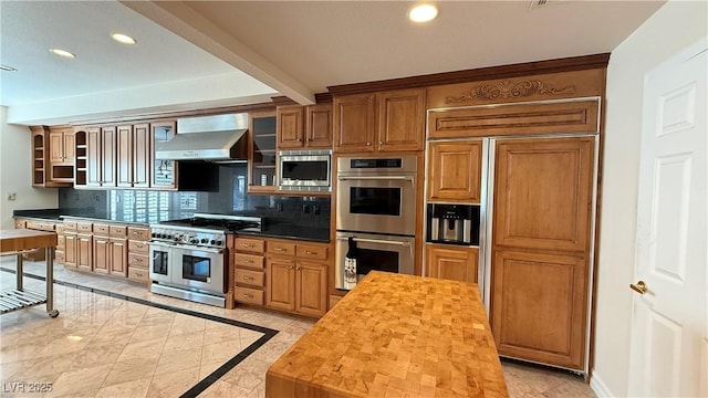 kitchen with wall chimney range hood, wooden counters, backsplash, built in appliances, and light tile patterned flooring