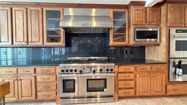 kitchen featuring appliances with stainless steel finishes, backsplash, dark stone countertops, and wall chimney range hood