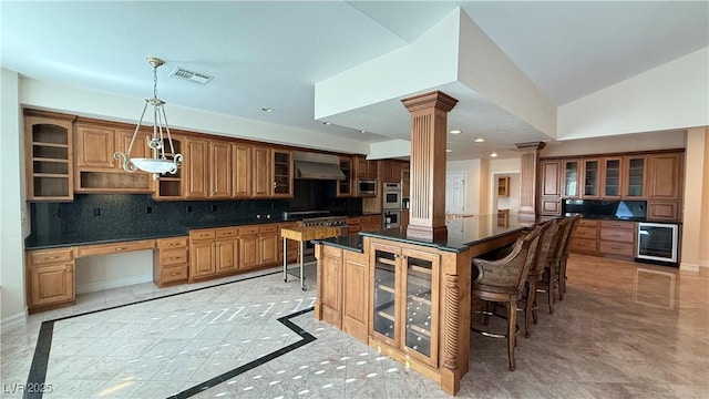 kitchen featuring backsplash, wall chimney range hood, ornate columns, decorative light fixtures, and beverage cooler