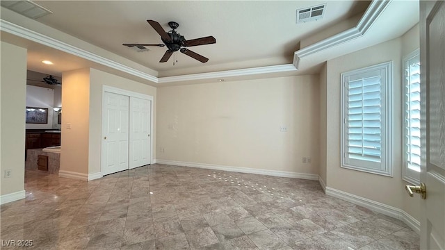 unfurnished bedroom with a tray ceiling, ceiling fan, crown molding, connected bathroom, and a closet