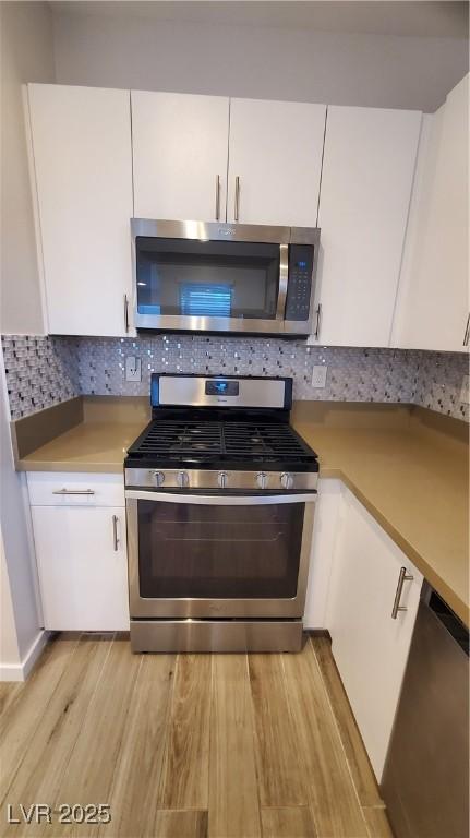 kitchen with white cabinets, appliances with stainless steel finishes, backsplash, and light wood-type flooring