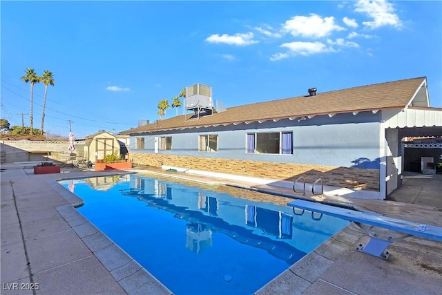 view of swimming pool featuring a patio, a shed, a diving board, and central air condition unit