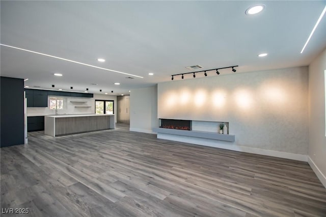 unfurnished living room with hardwood / wood-style floors, track lighting, and sink