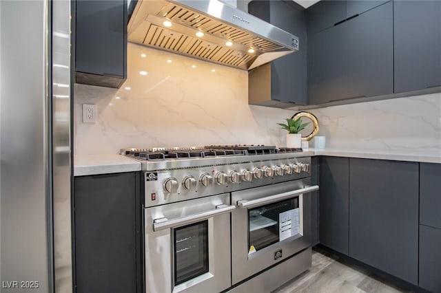 kitchen featuring backsplash, wall chimney exhaust hood, light hardwood / wood-style floors, and range with two ovens