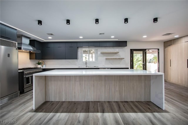 kitchen with light wood-type flooring, backsplash, high end appliances, wall chimney range hood, and a kitchen island