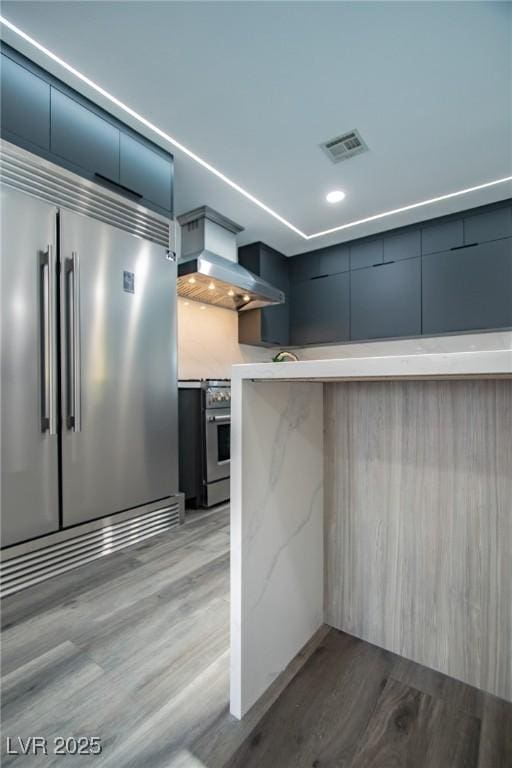 kitchen with stainless steel appliances, wall chimney range hood, and light wood-type flooring