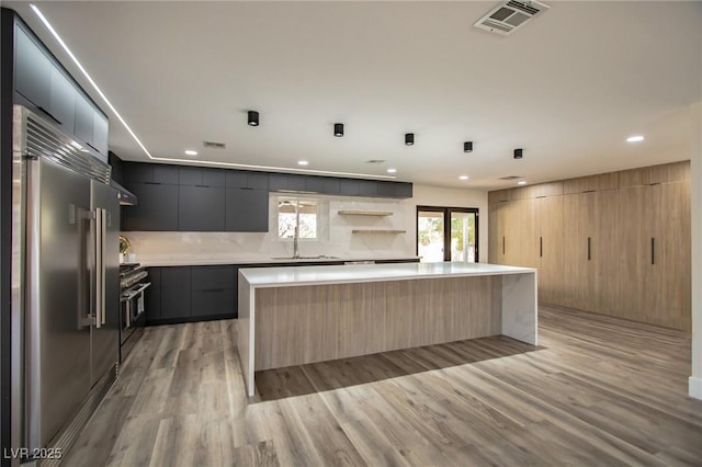 kitchen with a center island, light brown cabinets, stainless steel appliances, light hardwood / wood-style flooring, and decorative backsplash