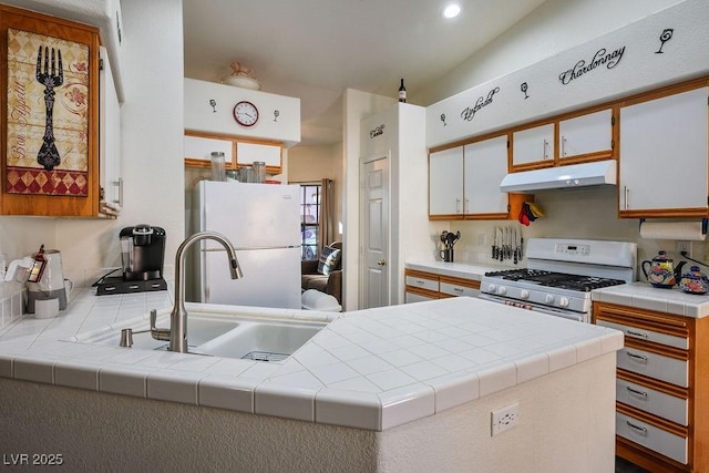 kitchen with tile countertops, kitchen peninsula, white cabinets, and white appliances