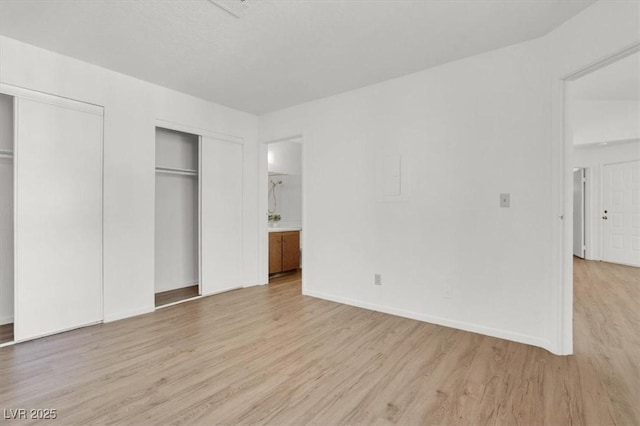 unfurnished bedroom with ensuite bathroom, two closets, and light wood-type flooring