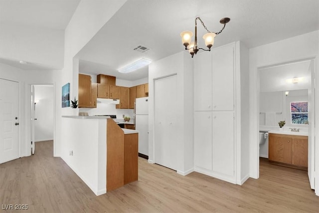 kitchen featuring hanging light fixtures, light hardwood / wood-style floors, a notable chandelier, and white refrigerator