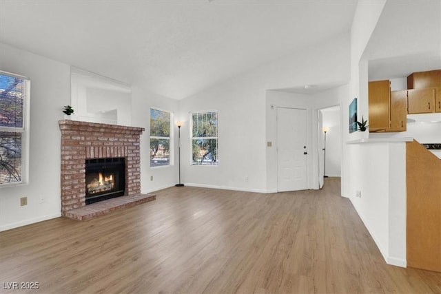 unfurnished living room featuring vaulted ceiling, light wood-type flooring, and a brick fireplace