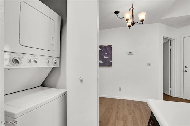 laundry room featuring light wood-type flooring, an inviting chandelier, and stacked washer / dryer