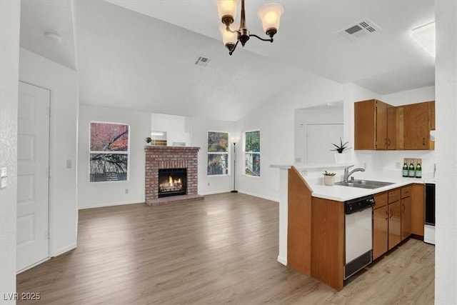 kitchen with kitchen peninsula, a brick fireplace, dishwashing machine, sink, and a chandelier