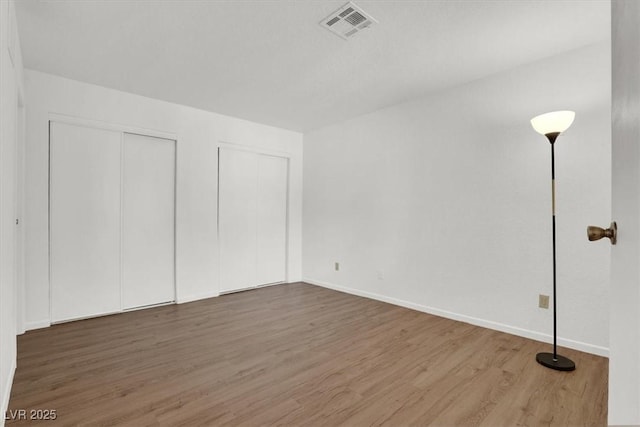 unfurnished bedroom featuring hardwood / wood-style flooring and multiple closets