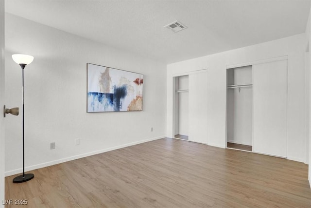 unfurnished bedroom featuring two closets and hardwood / wood-style flooring