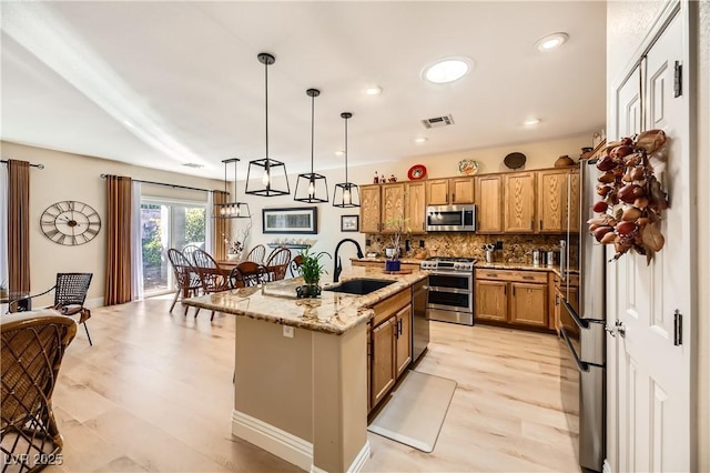 kitchen featuring a center island with sink, sink, hanging light fixtures, appliances with stainless steel finishes, and light stone counters