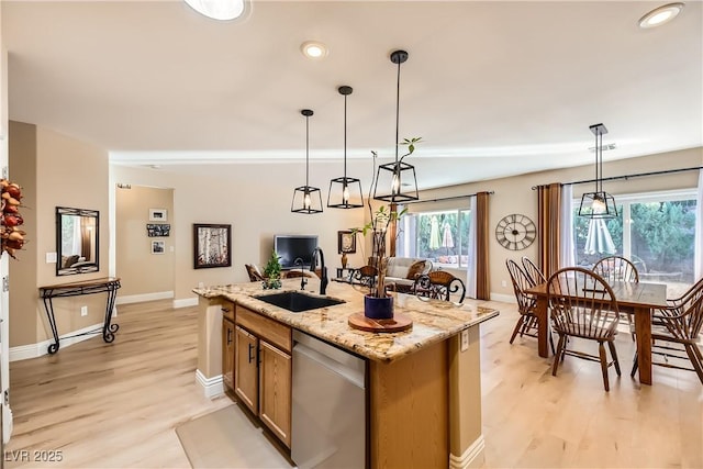 kitchen featuring light stone countertops, stainless steel dishwasher, sink, pendant lighting, and a center island with sink