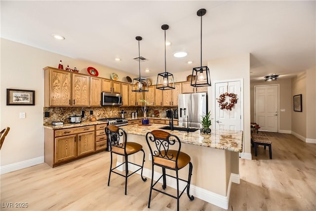 kitchen with pendant lighting, a kitchen island with sink, appliances with stainless steel finishes, light stone counters, and a breakfast bar area